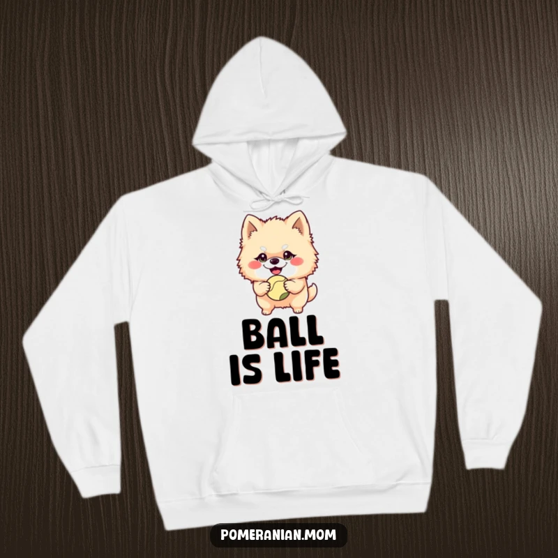 Funny Pomeranian character with a mischievous grin holding a ball on this cozy hoodie, radiating playful intent and energetic fun.